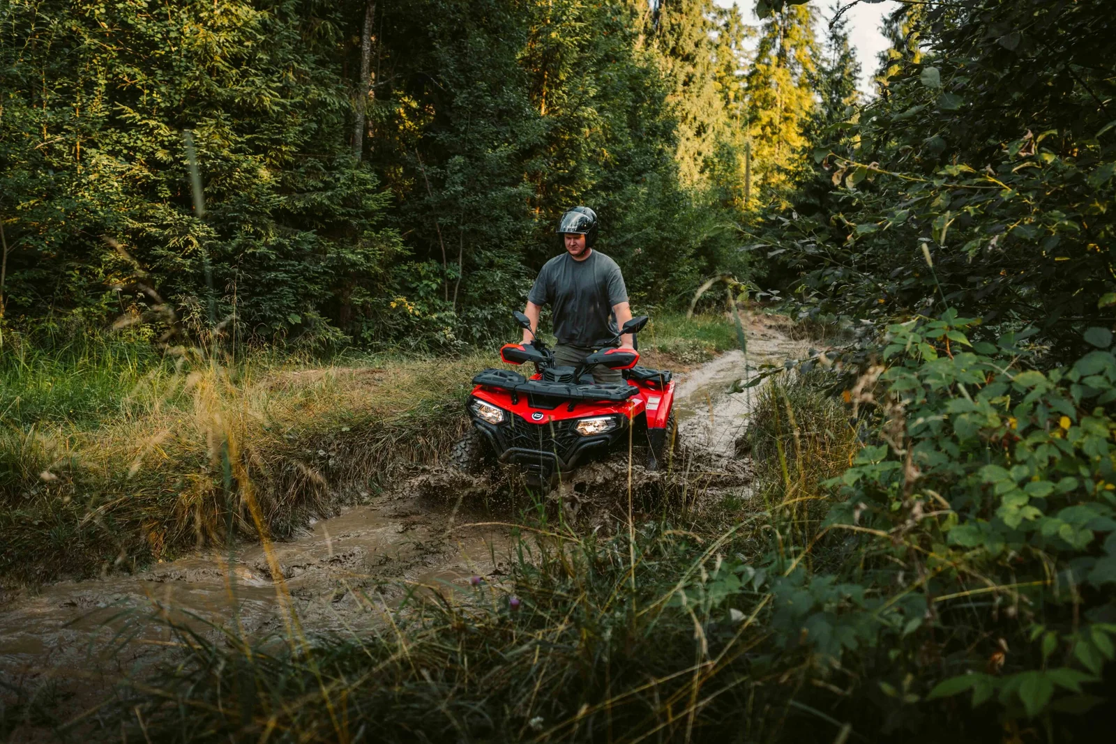 ZDJ-02025 – czerwony quad z kierowcą pokonujący głębokie błoto na wąskiej leśnej trasie