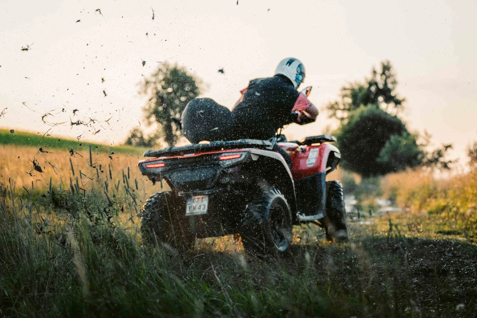 ZDJ-02393 – czerwony quad widziany od tyłu podczas dynamicznej jazdy przez błoto o zachodzie słońca