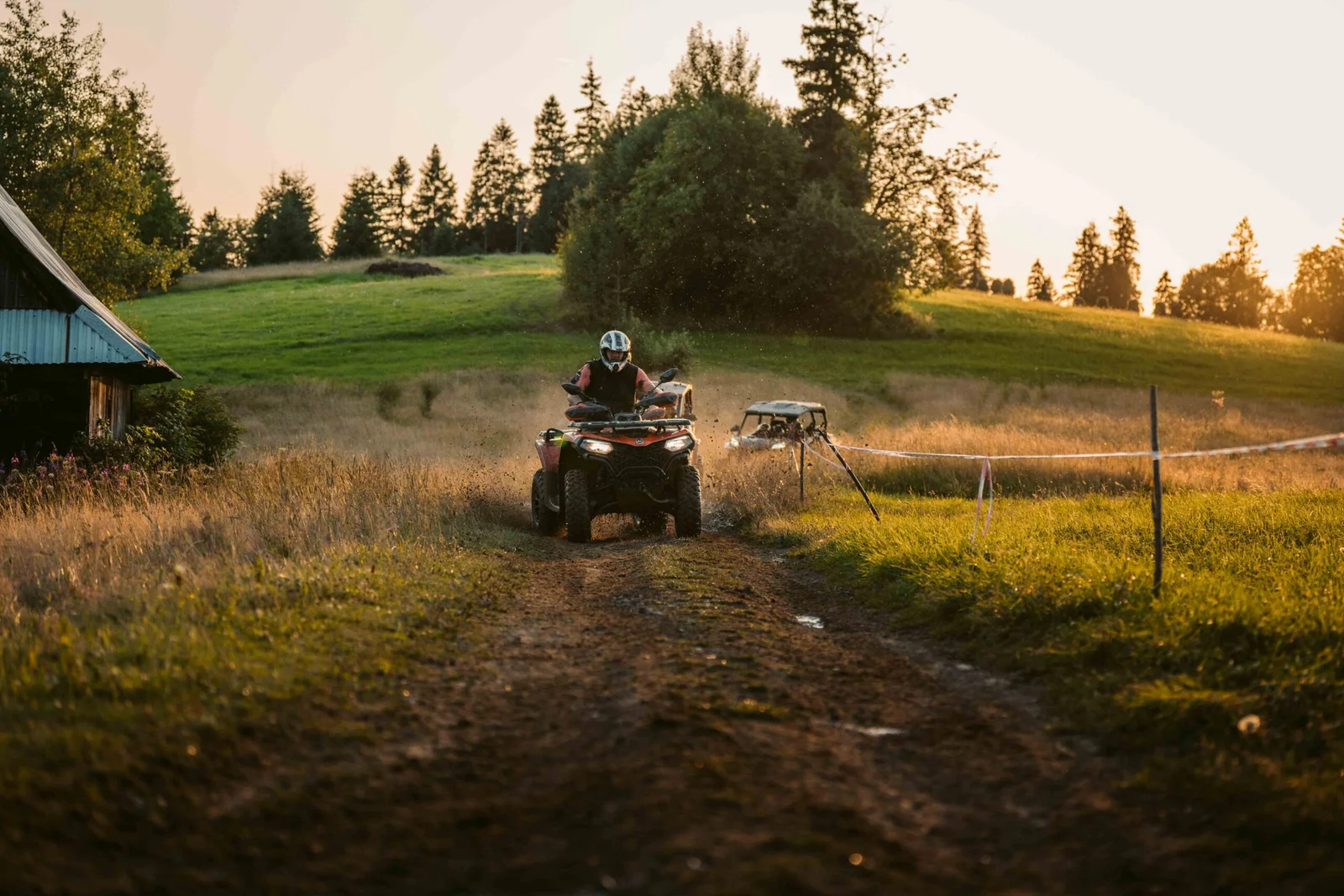 ZDJ-02624 – czerwony quad jadący w stronę aparatu polną trasą o zachodzie słońca, buggy w tle